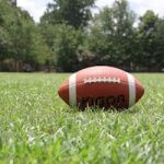 A close-up of an American football on a grassy field, highlighting outdoor sports in summer.
