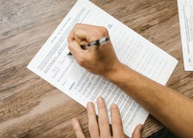 pexels-photo-7821686-7821686 Person filling out a tax questionnaire with a pen, showing close-up on wooden table.