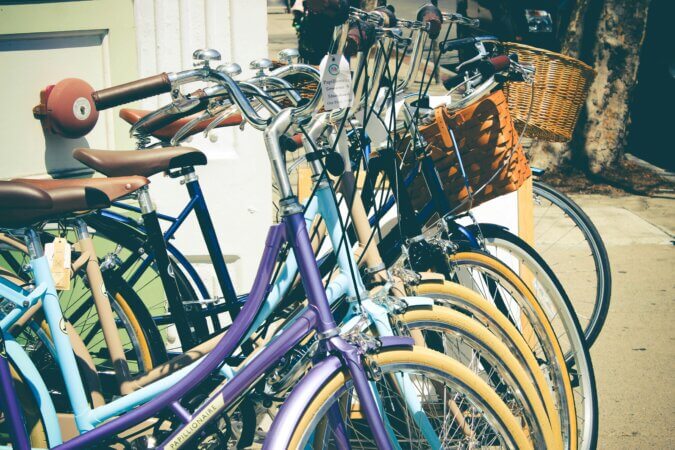 A row of colorful vintage bicycles with baskets parked on a sunny street, perfect for outdoor and lifestyle themes.